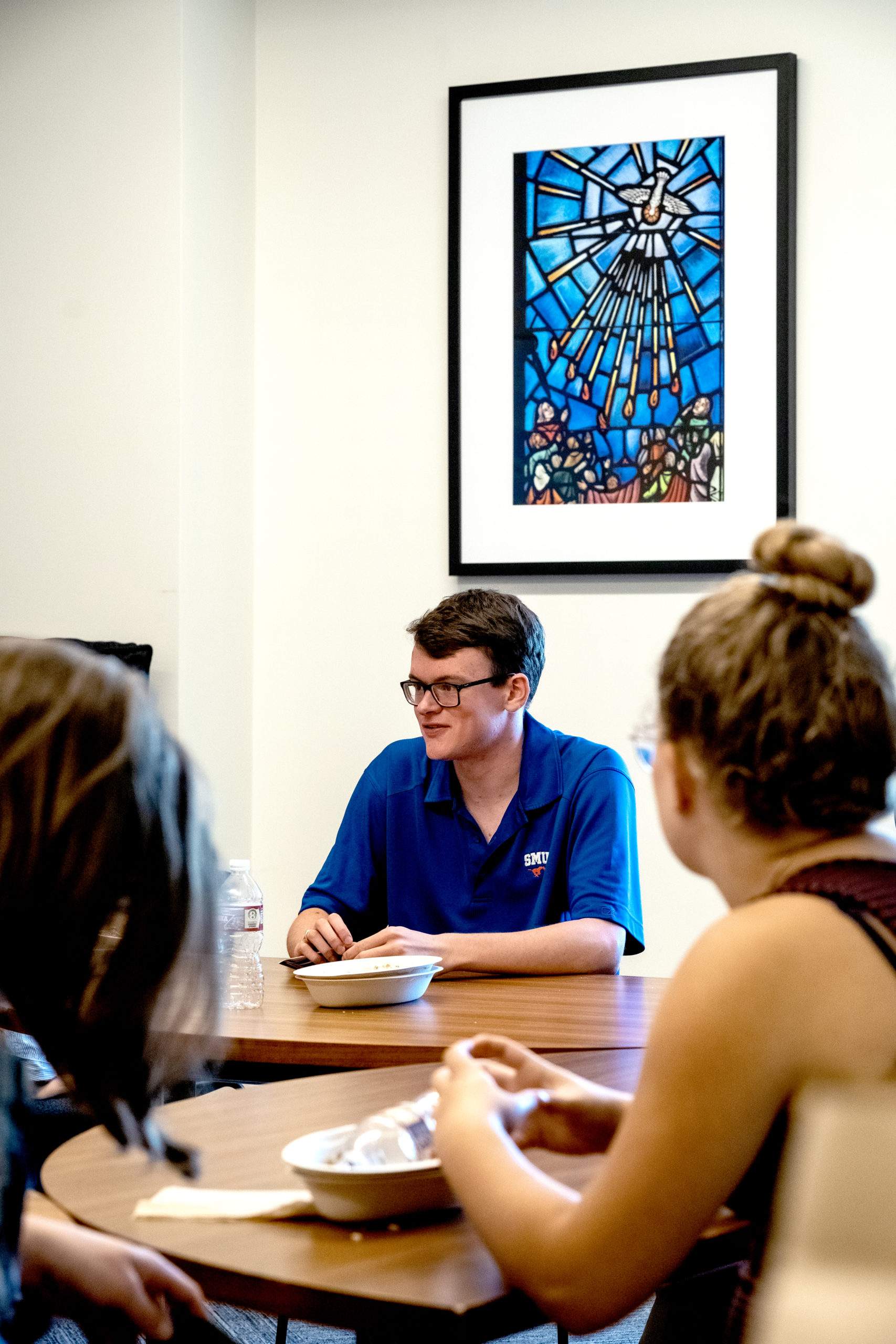 Student in blue shirt with glasses talking at a table